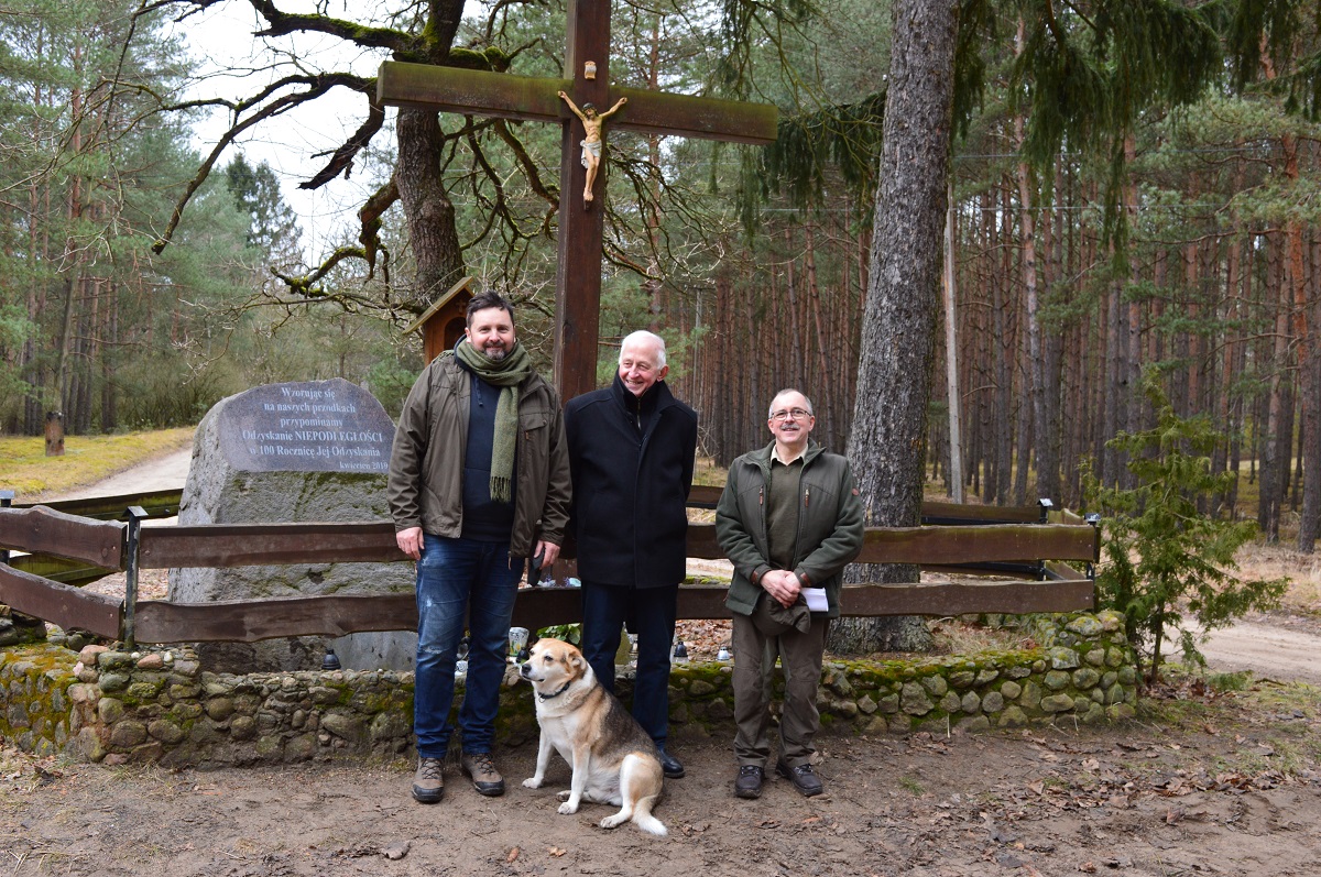 Zdjęcie przedstawia wnuka leśniczego Tomasza Andrzejewskiego Pana Waldemara Kozłowskiego (w środku) w towarzystwie obecnego leśniczego Leśnictwa Gogolice, Nadleśnictwo Wronki, Macieja Grupy (z lewej) i pasjonata historii z Nadleśnictwa Sieraków Romana Tomczaka (z prawej) przy dwóch kamieniach upamiętniających Niepodległość Polski (fot. Roman Tomczak Nadleśnictwo Sieraków)